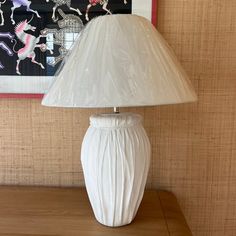 a white lamp sitting on top of a wooden table next to a framed picture and painting