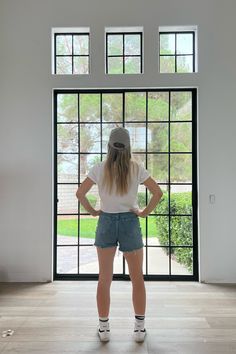 a woman standing in front of a large window with her back to the camera and hands on hips