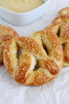 three pretzels sitting next to a bowl of dip on a white tablecloth