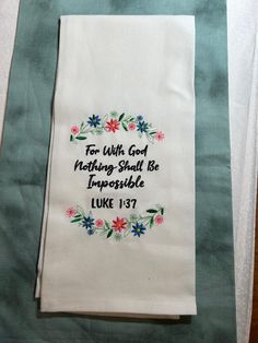 embroidered tea towel with bible verse on it sitting on top of a blue table cloth