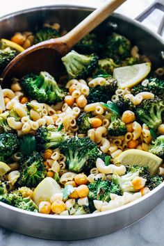 a pan filled with pasta, broccoli and lemon wedges