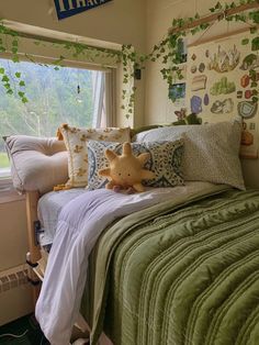 a bed with green comforter and pillows in a small room next to a window