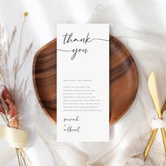 a thank card on top of a wooden plate next to some dried flowers and gold utensils