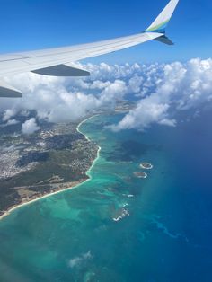 an airplane wing flying over the ocean with clouds and land in the foreground below