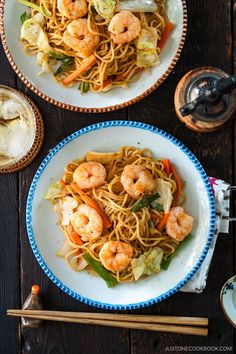 two plates with noodles and shrimp on them next to chopsticks, water glass and utensils