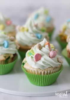 cupcakes with white frosting and colorful candies on top are arranged on a plate