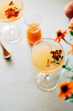 two glasses filled with drinks sitting on top of a table next to oranges and flowers