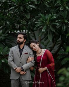 a man and woman standing next to each other in front of some trees with green leaves