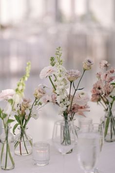 several vases filled with different types of flowers on a white tablecloth covered table