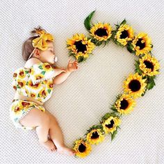 a baby laying in the shape of a heart with sunflowers