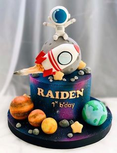 a cake with an astronaut on top of it and planets around the base that says raden 1st birthday