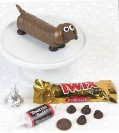 a chocolate dog on top of a white cake plate next to candy and candies