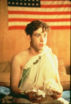 the young man is sitting in front of an american flag and holding a bouquet of flowers