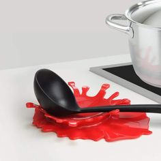 a spoon with red liquid on it sitting next to a saucepan and spatula