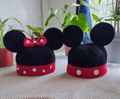 two crocheted mickey mouse hats sitting on top of a table next to a potted plant