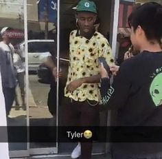 a man standing in front of a glass door talking to another person wearing a green hat