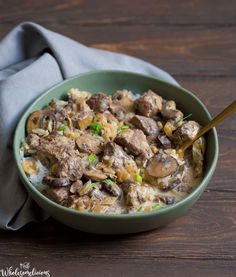 a green bowl filled with meat and mushrooms on top of a wooden table next to a gray napkin