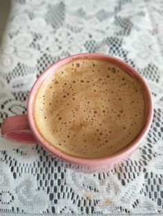 a cup of coffee sitting on top of a lace covered table cloth with the lid down