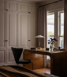 a bedroom with a desk and chair next to a window that has curtains on the windowsill