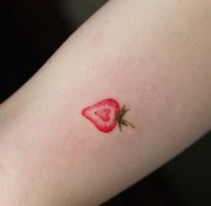 a heart shaped strawberry tattoo on the left arm with a small red flower in it