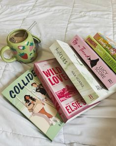 a stack of books sitting on top of a bed next to a cup and bookend