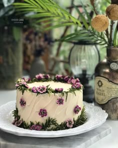 a white cake with purple flowers on it sitting on a plate next to some vases