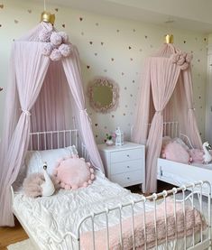 two white beds with pink curtains in a girls'bedroom, one has a teddy bear on the bed