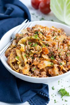 a white bowl filled with pasta and meat on top of a blue napkin next to tomatoes