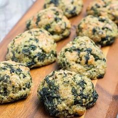 a wooden cutting board topped with lots of green food covered in cheese and spinach