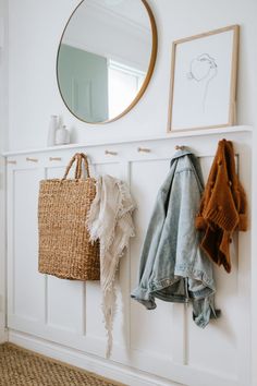 two coats hanging on the wall next to a mirror and coat rack in a white room