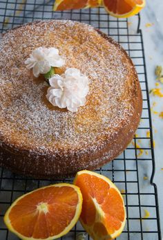 an orange cake with powdered sugar on top and sliced oranges next to it