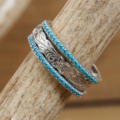 two rings with turquoise beads are sitting on a piece of wood and one ring has a silver filigree