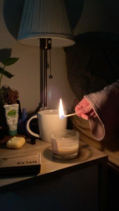 a person lighting a candle on a table next to a bowl and cup with something in it