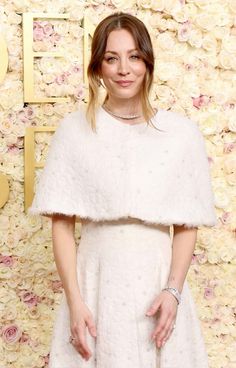 a woman standing in front of a flower wall wearing a white dress and diamond bracelets