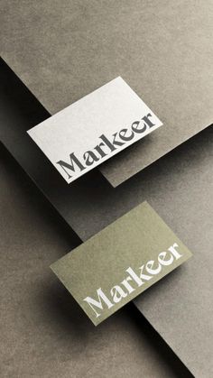 two business cards sitting next to each other on top of gray paper with white lettering