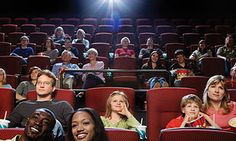 group of people sitting in an auditorium with red seats and one person smiling at the camera