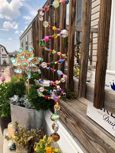 a colorful wind chime hanging from the side of a wooden fence next to potted plants