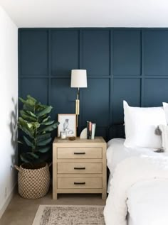 a bed room with a neatly made bed next to a night stand and a plant