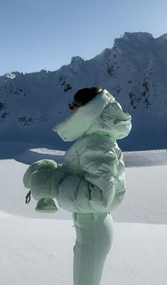 a woman standing in the snow with her back to the camera, wearing a green coat