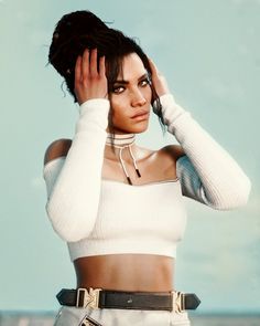 a woman in white top and black belted skirt posing with her hands on her head