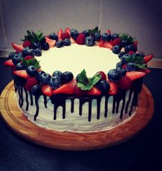 a white cake with berries and chocolate drizzled on top is sitting on a wooden platter