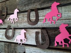 pink and brown paper cutouts are hung on a wooden wall with horseshoes hanging from them