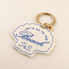 a white keychain with blue writing on it that says let's go to the beach