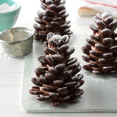 three small pine cones sitting on top of a cutting board covered in powdered sugar