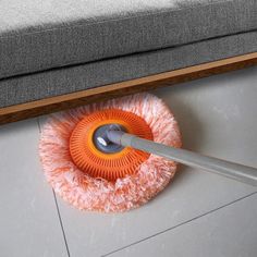 an orange mop laying on top of a floor next to a gray couch with a wooden frame