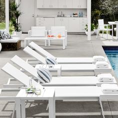 an outdoor pool with lounge chairs and tables next to the swimming pool in front of it