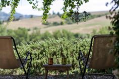 two lawn chairs sitting next to each other on top of a gravel field with trees in the background