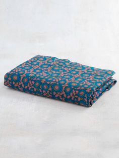 a blue and pink blanket laying on top of a white surface with an orange flower pattern