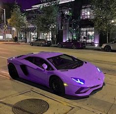 a purple sports car is parked on the side of the road at night in front of a building