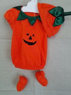 an orange halloween outfit with a green bow on the neck and matching slippers is laying on a white sheet